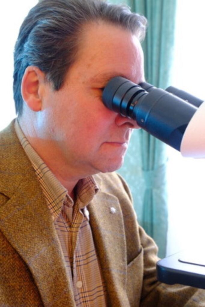 Marco Beitelberger blickt konzentriert durch das Okular eines Mikroskops bei einer Dunkelfeldmikroskopie Wien Untersuchung.