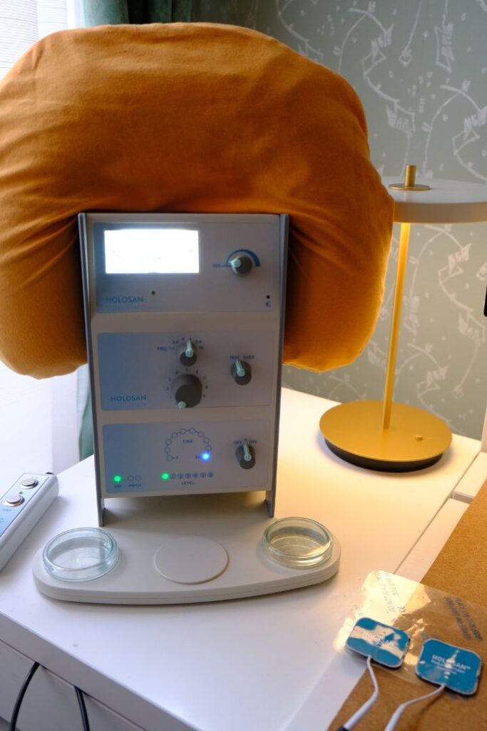 Ein HOLOSAN Bioresonanzgerät mit Bedienfeld, Reglern und Leuchtdioden auf einem weißen Tisch. Diese Technologie kommt im Rahmen der Darmsanierung in Wien zur Testung von Nahrungsmittelunverträglichkeiten zum Einsatz.