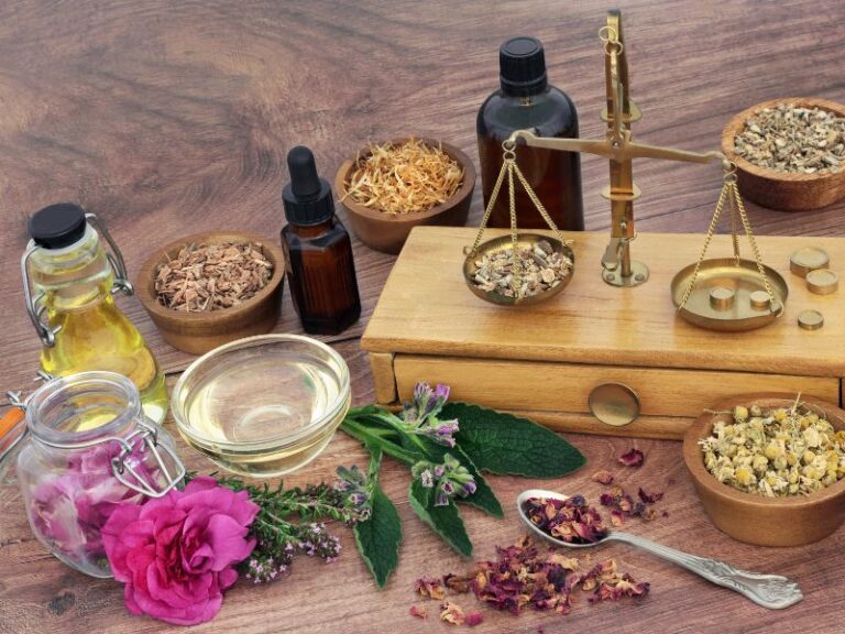 Apothekerwaage aus Messing umgeben von Schalen mit Heilkräutern, Flaschen mit Tinkturen, Ölen und frischen Pflanzen auf einem Holztisch, repräsentativ für die Arbeit in der Naturheilpraxis in Wien.