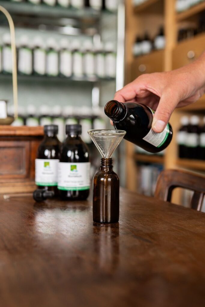 Eine Hand gießt vorsichtig eine dunkle pflanzliche Essenz durch einen Glastrichter in eine kleine braune Apothekerflasche. Mit solchen individuellen Rezepturen unterstützen wir Sie in Wien dabei, Ihre Leistungsfähigkeit zu steigern.