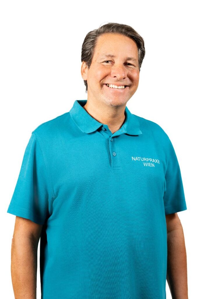 Porträt von Mag. pharm. Marco Beitelberger in einem türkisfarbenen Poloshirt mit dem Logo der Naturpraxis Wien. Er bietet ganzheitliche Naturheilkunde in Wien an.